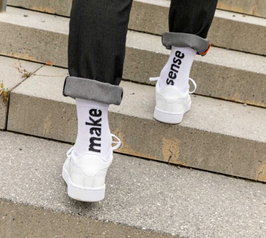 Close up from behind of male feet walking up urban stairs with black jeans, white socks.