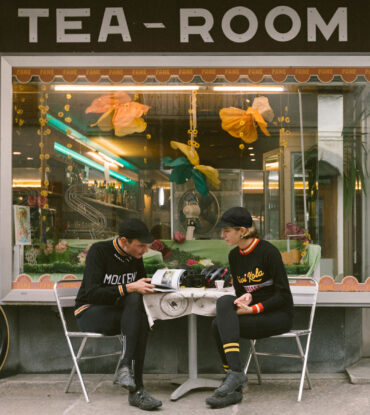 Two bike riders drinking coffee at a Tea Room.